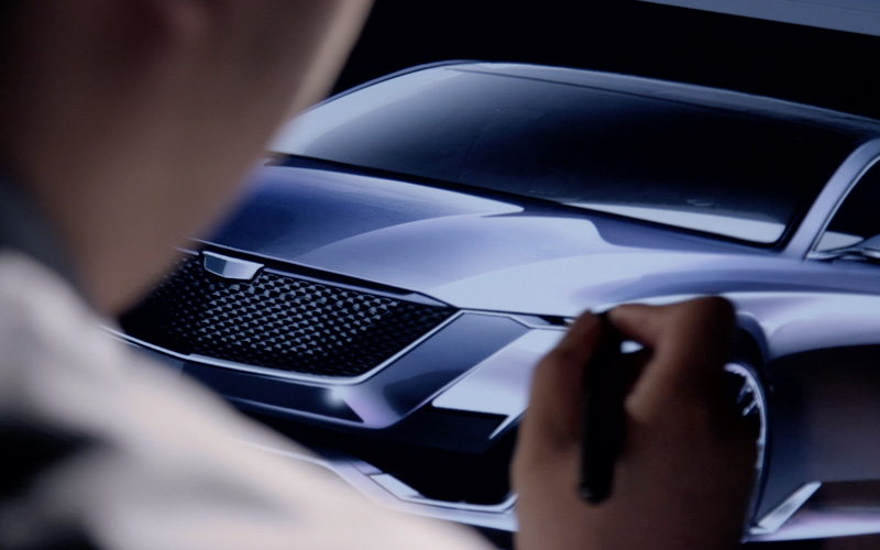 A man holds a digital pen drawing on a screen with the image of a silver concept car.